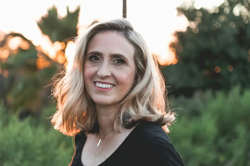 A smiling woman with silver-blonde hair in golden evening light