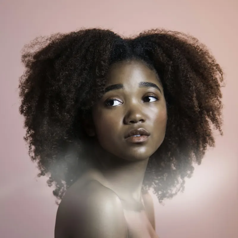 A woman with voluminous natural coils against a blush background