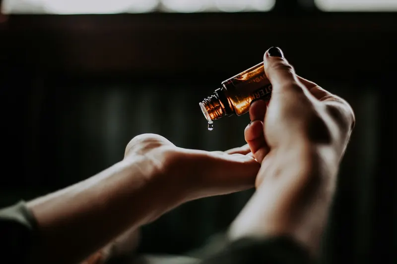 A hand holding an amber dropper bottle, a drop of oil falling into the palm