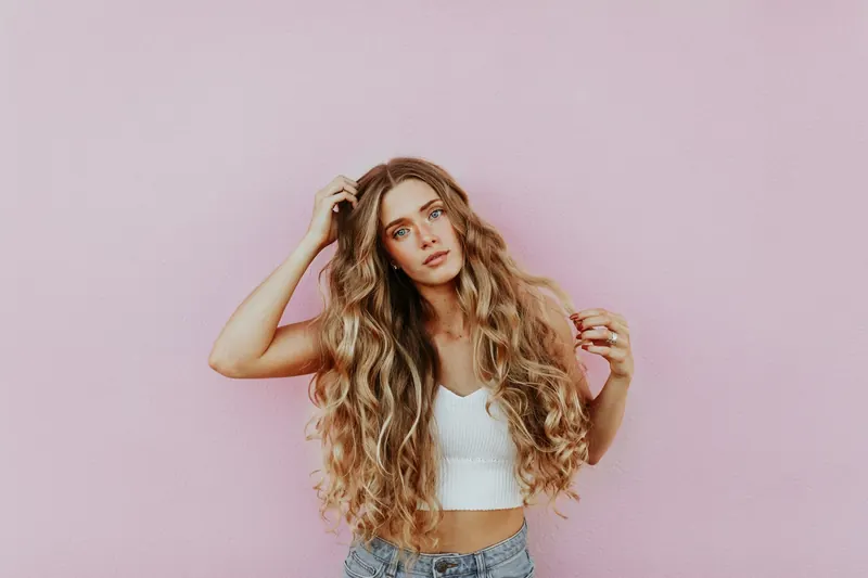 A woman with long, heatless wavy blonde hair against a pink wall