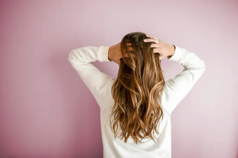 A woman with long, glossy brown waves running her hands through her hair