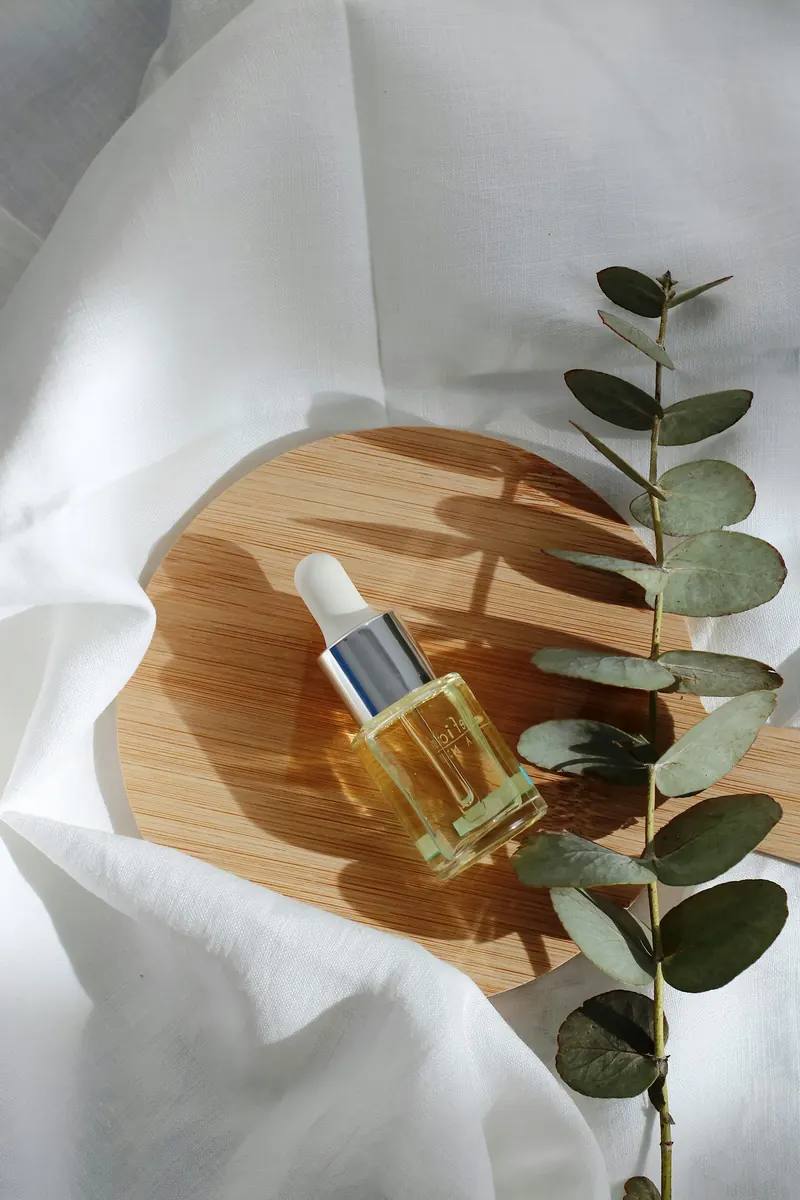 A glass serum bottle with a dropper on a wooden tray beside eucalyptus